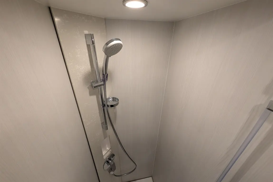 Shower area featuring a modern chrome showerhead, tiled wall, and control panel, creating a sleek design.