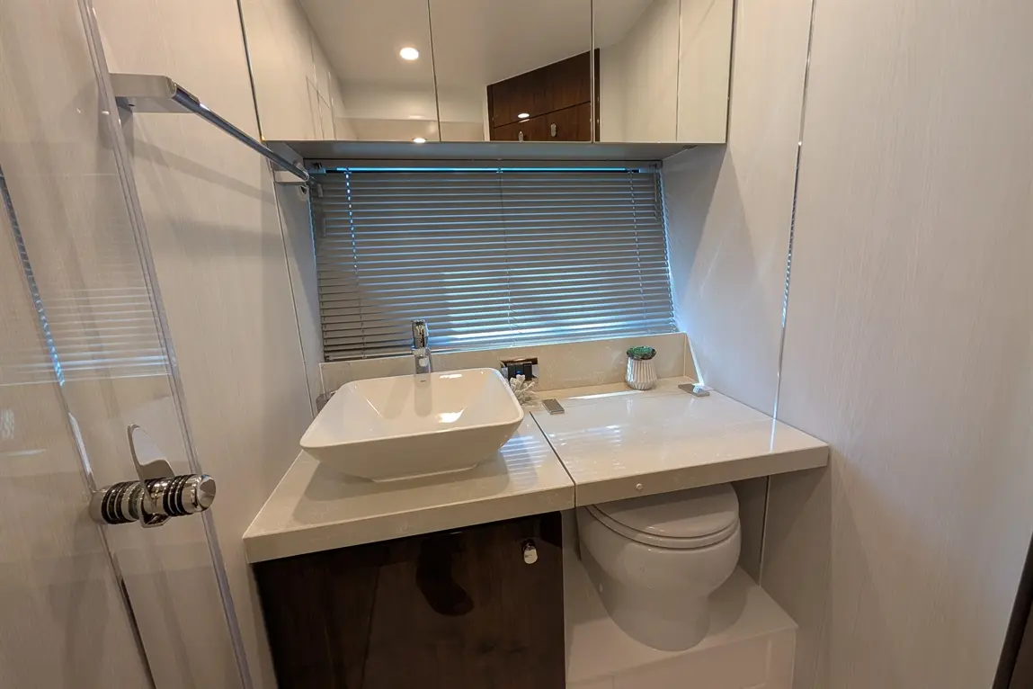 Modern bathroom featuring a white sink, toilet, and a wooden cabinet, with horizontal blinds and overhead mirrors.