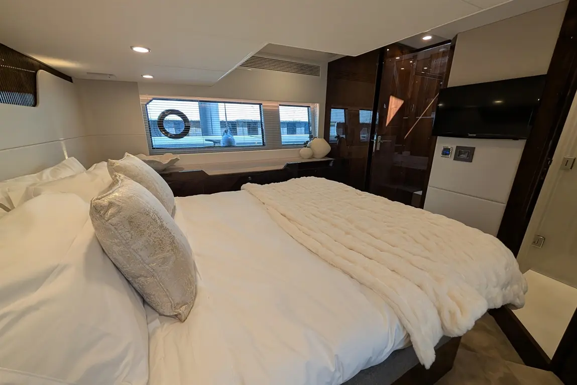 Luxurious bedroom with a plush white blanket and pillows, large window, and modern TV, showcasing elegant interior design.