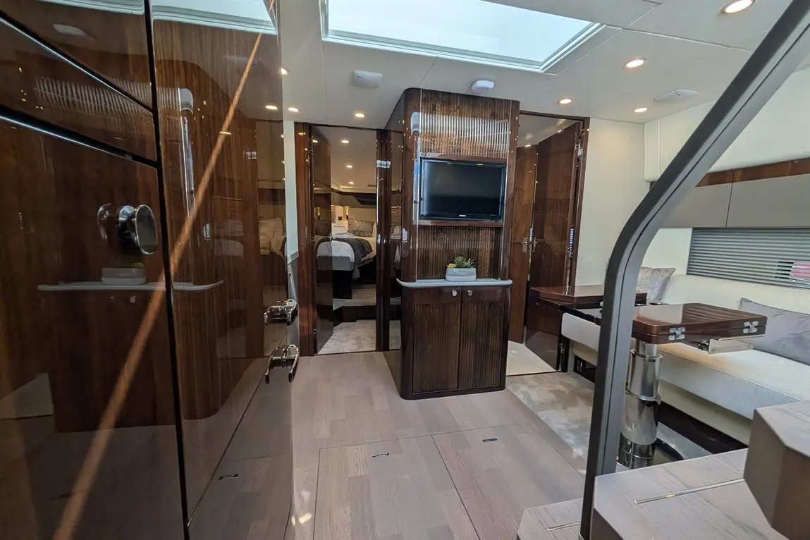 Luxurious yacht interior featuring wooden panels, a television, and a skylight, leading to a bedroom area.