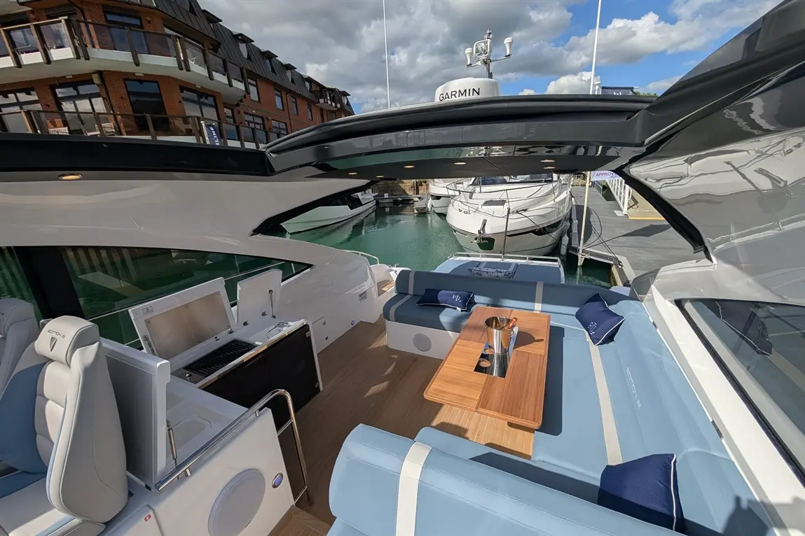 Interior of a modern boat with plush seating, a dining table, and a visible Garmin device, docked by luxury yachts.