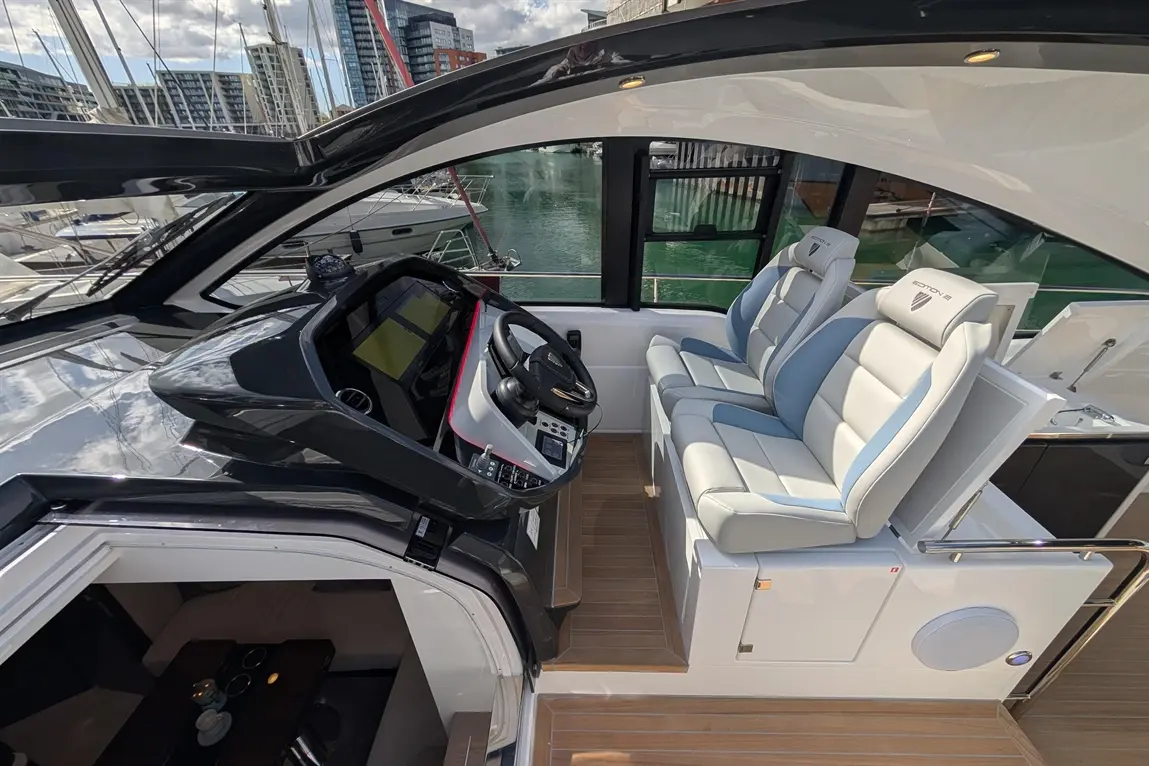 Luxury boat interior featuring sleek dashboard, steering wheel, and plush seating in sunlit marina setting.