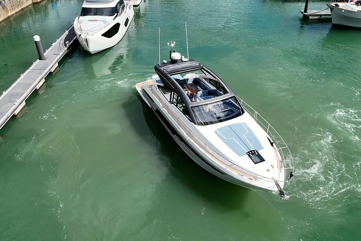 A white motorboat manoeuvres in green waters near a dock, showcasing sleek design and a sunny environment.