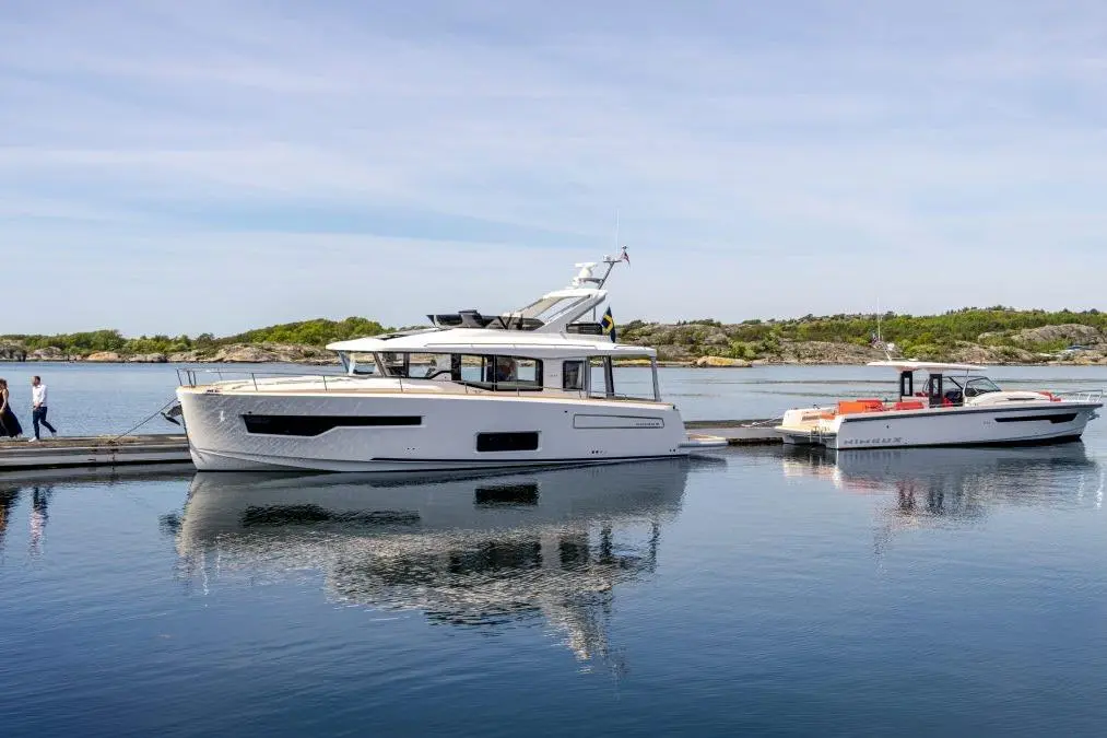 Two boats docked at a peaceful marina, with a clear sky above and green islands in the background, reflecting in the water.