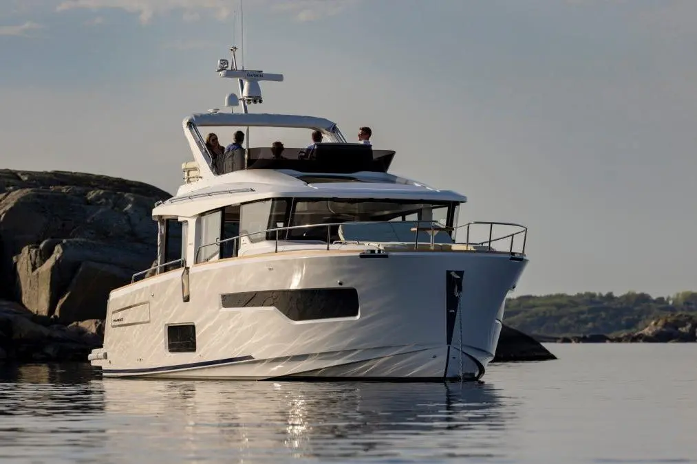 A luxurious yacht anchored on calm waters, with people enjoying time on the deck against a scenic coastal backdrop.