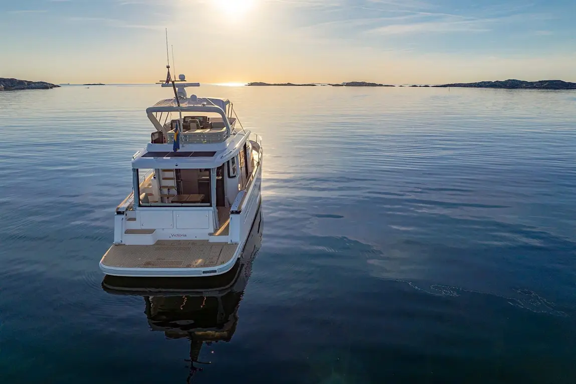A white motorboat named "Victoria" floats on calm waters during sunset, with rocky islands in the distance.