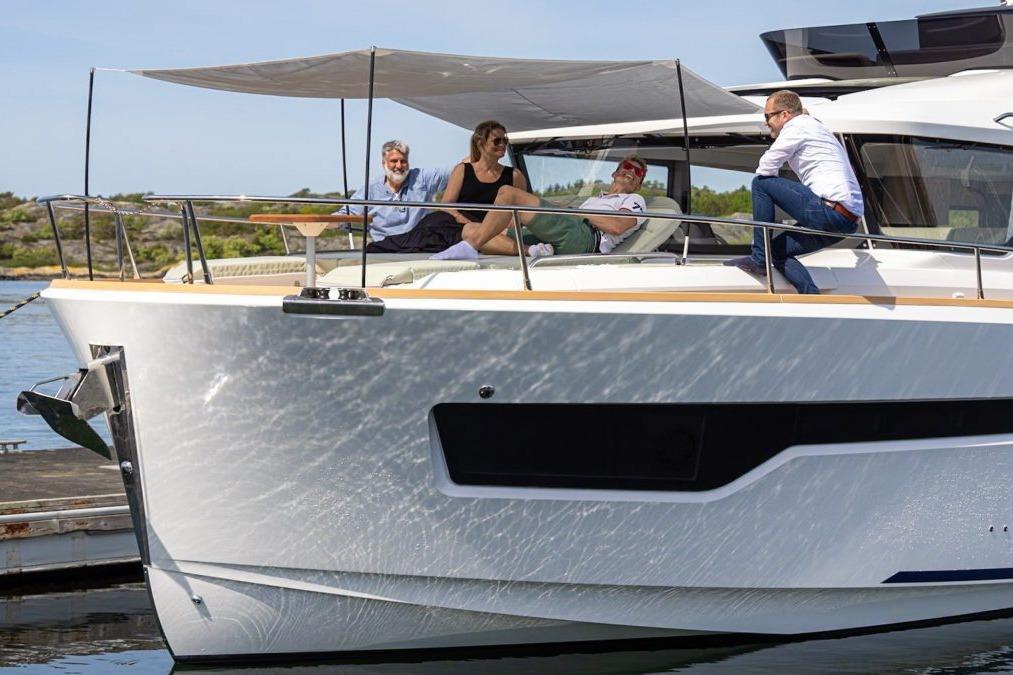Four people relax on a modern yacht, enjoying the sun and water, with a scenic backdrop of greenery and blue sky.
