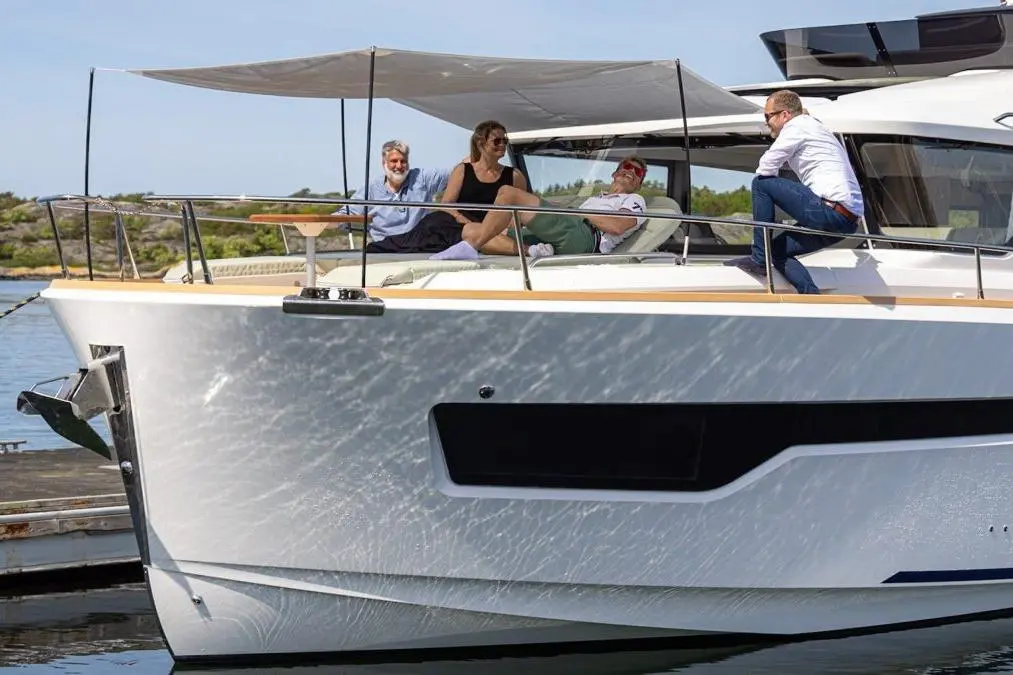Four people relax on a modern yacht, enjoying the sun and water, with a scenic backdrop of greenery and blue sky.