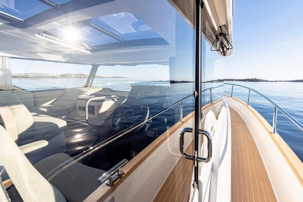 Modern boat interior with sleek seating, dashboard, and panoramic views of calm water and coastline under clear skies.