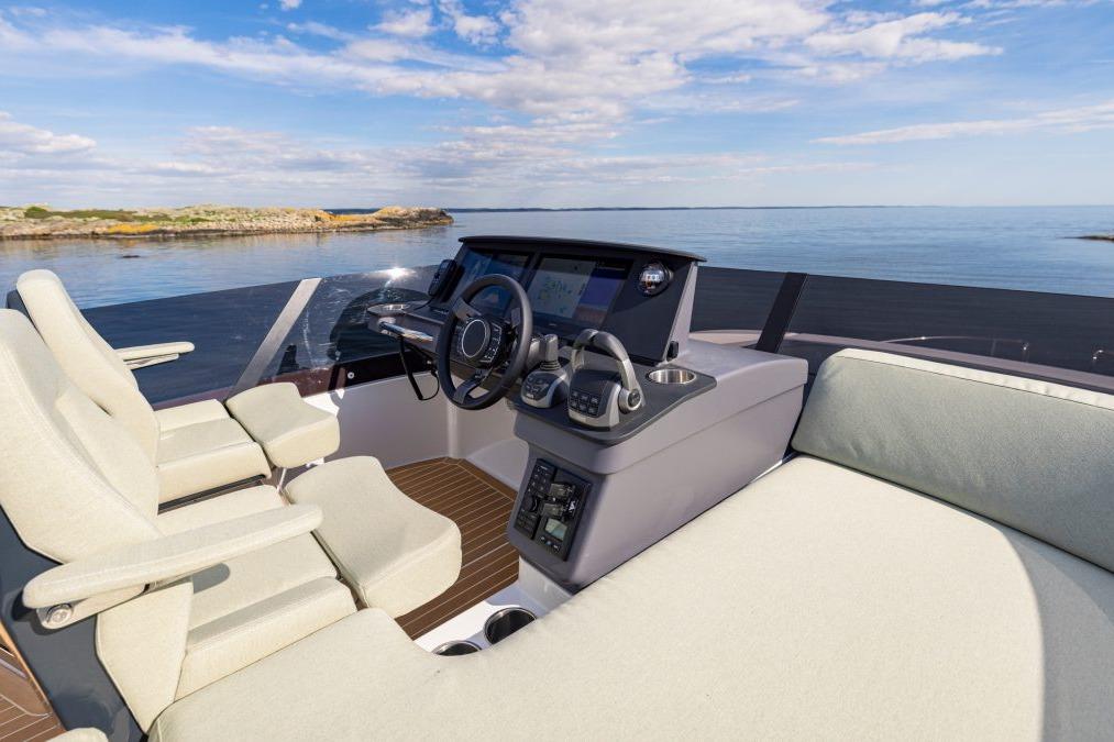 View of a modern boat's helm with two plush seats, a navigation display, and a serene water background under a blue sky.