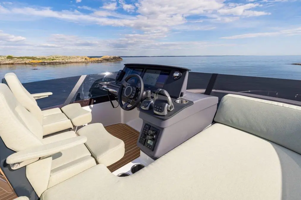 View of a modern boat's helm with two plush seats, a navigation display, and a serene water background under a blue sky.