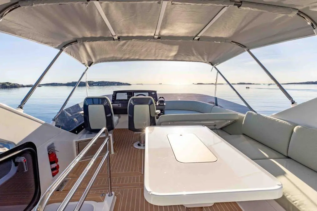 Interior of a modern boat with two seats and a table, overlooking calm water and distant islands under a clear sky.