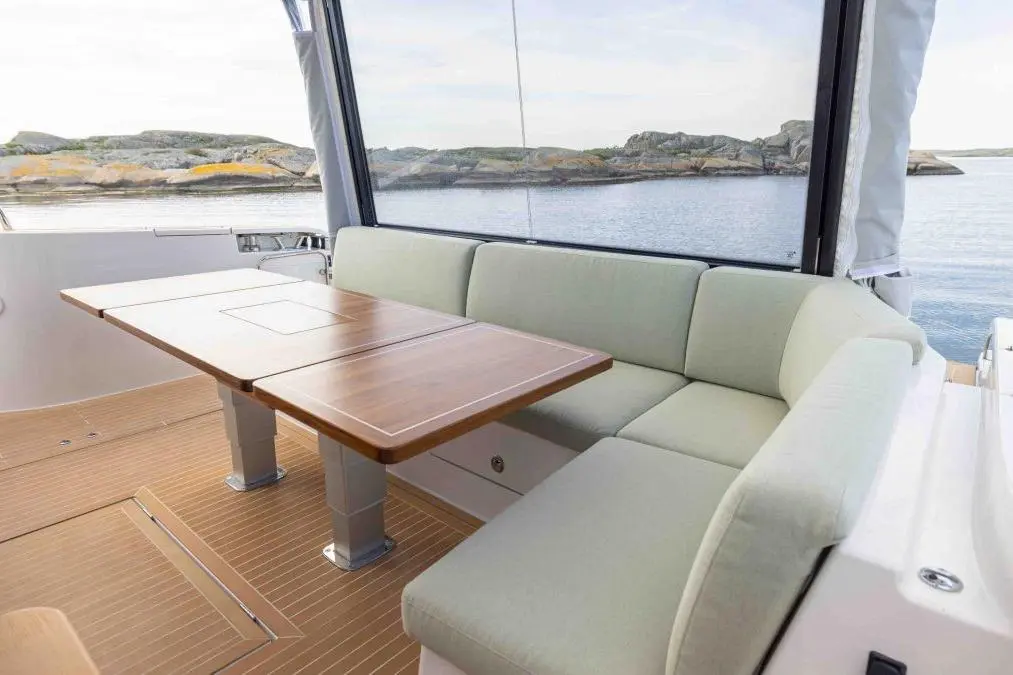 Cozy boat interior featuring a light green cushioned seat and wooden table, with a scenic waterfront view outside.