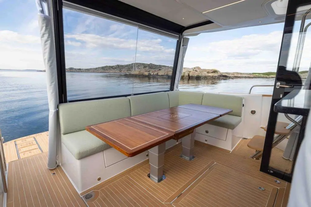 Modern boat interior featuring a wooden dining table, green cushioned seating, and scenic waterfront views.