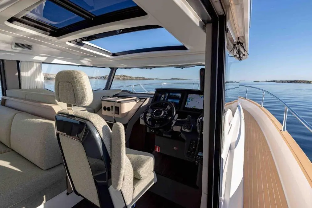 Interior view of a modern boat's cockpit with a steering wheel, navigation screen, and comfortable seating, overlooking calm waters.