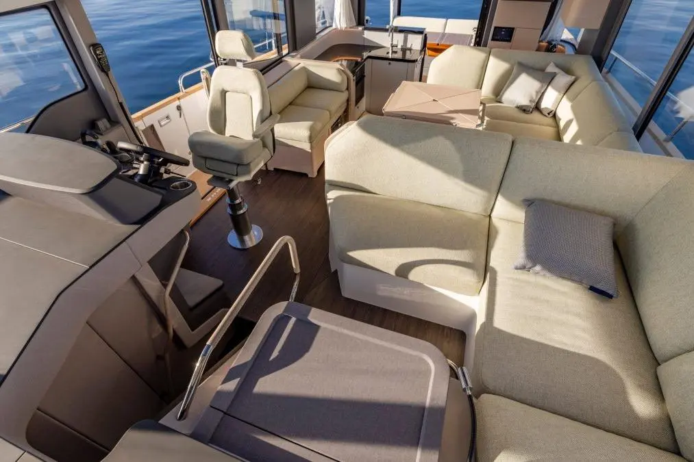 Modern yacht interior featuring a spacious lounge with light-colored seating, a helm with controls, and panoramic views.