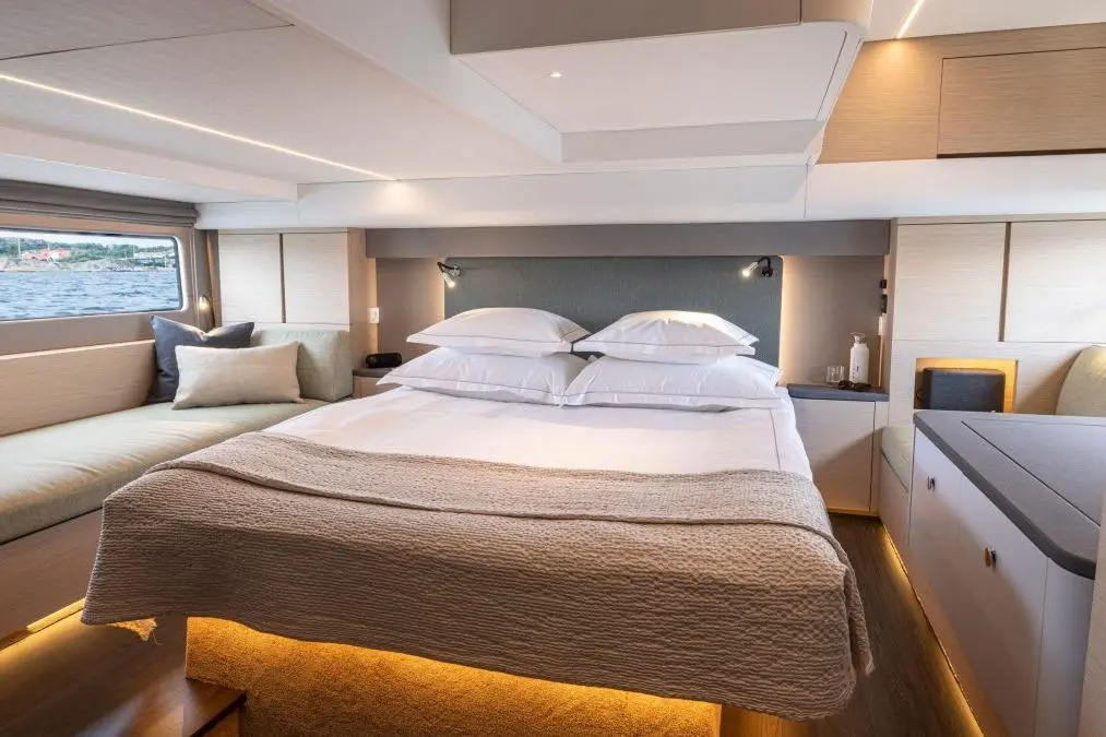 Modern yacht cabin featuring a queen-sized bed, soft lighting, a cozy seating area, and a view of the water outside.