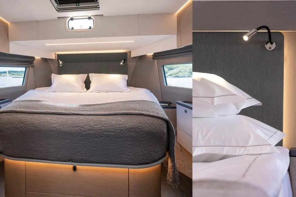 Modern boat cabin featuring a double bed with gray bedding, accent lighting, and a reading light on the wall next to a window.