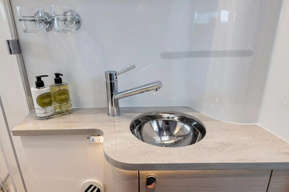 Modern bathroom sink area featuring a chrome faucet and soap dispensers with marble countertop and a stainless steel bowl.