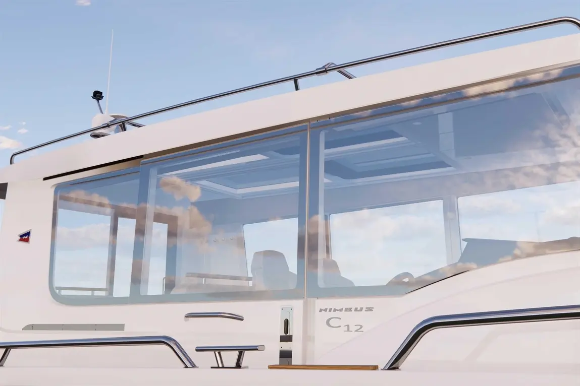 A close-up view of a Nimbus C12 boat's glass cabin, featuring sleek lines, stainless steel railings, and a clear sky reflection.