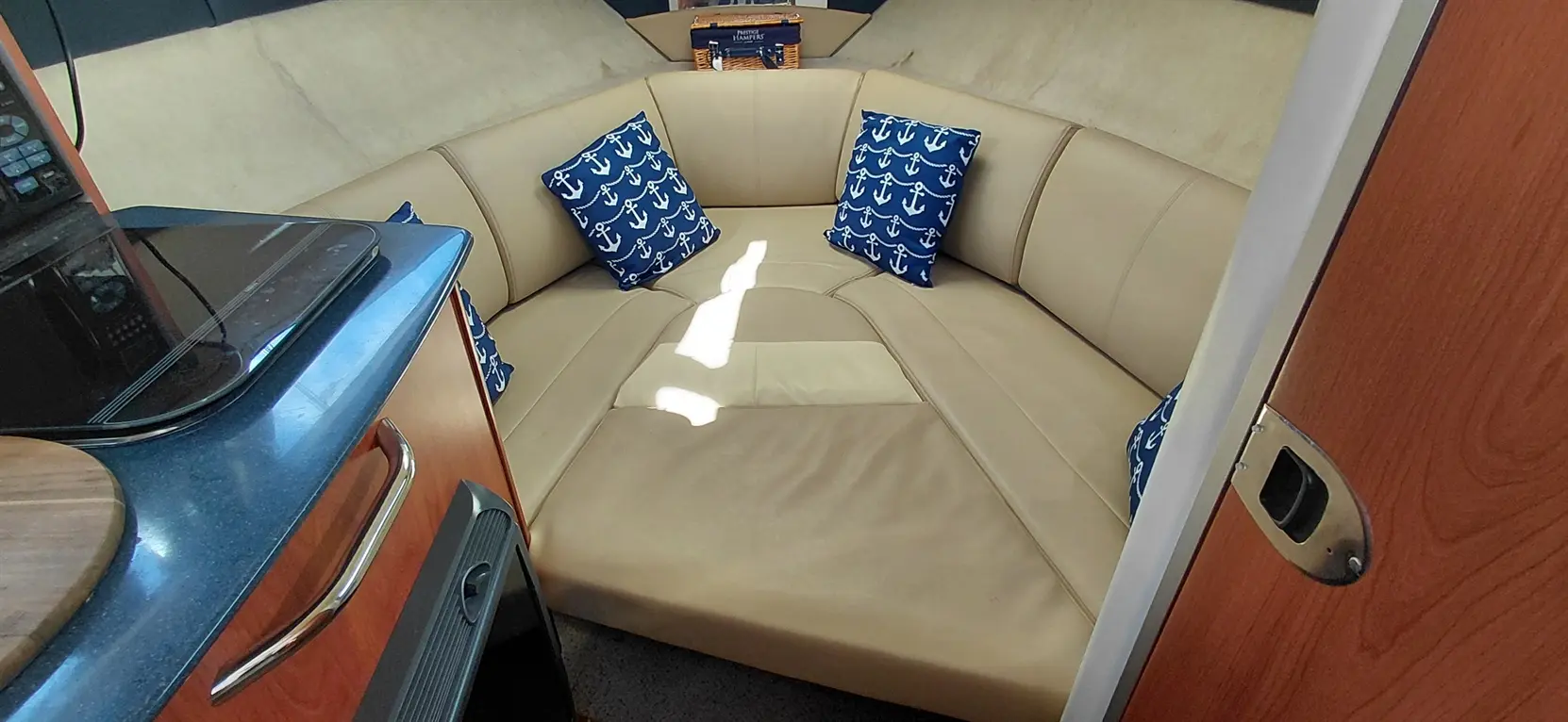 Interior of a boat featuring a beige seating area with blue anchor-patterned cushions and a countertop with kitchen items.