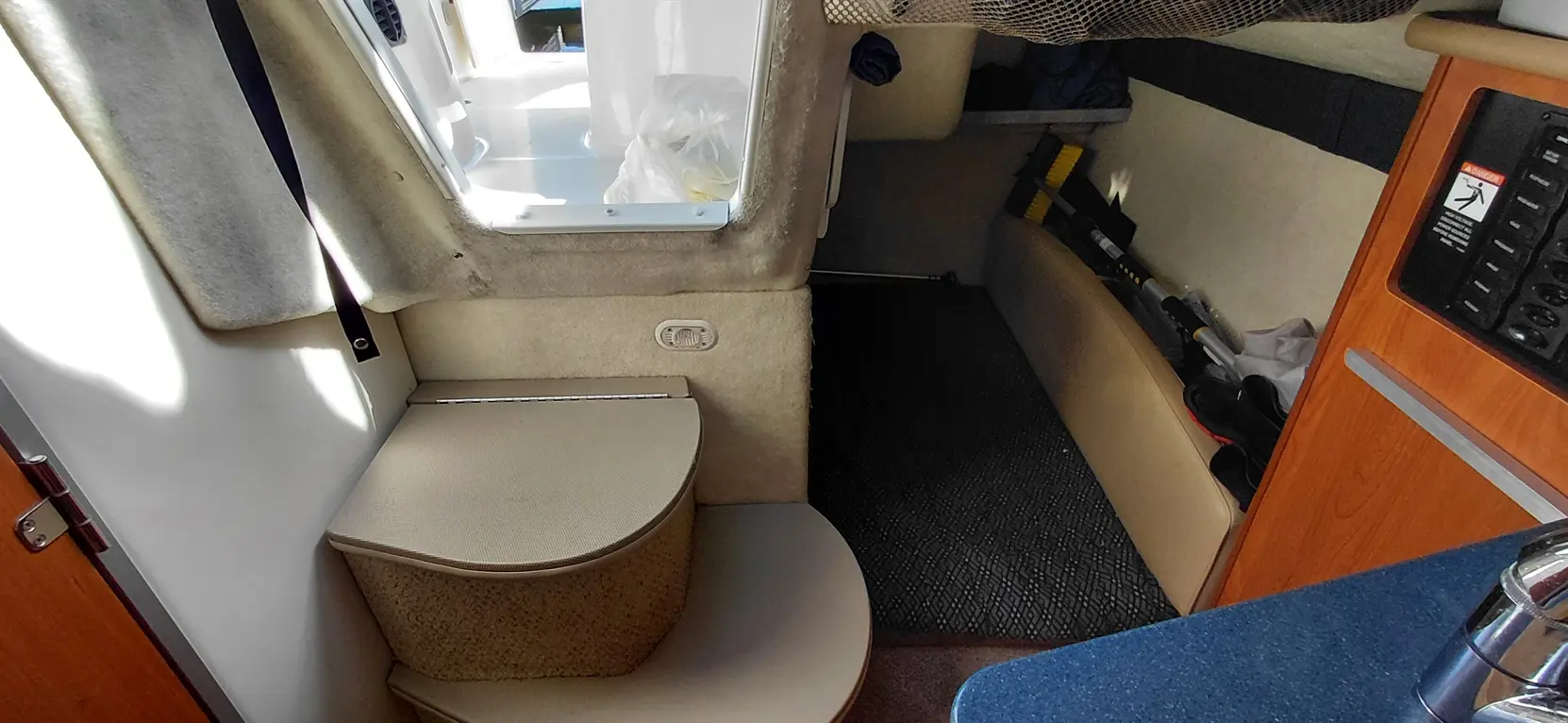 Interior view of a boat cabin showing a rounded seating area, storage, and a kitchenette with blue countertop.