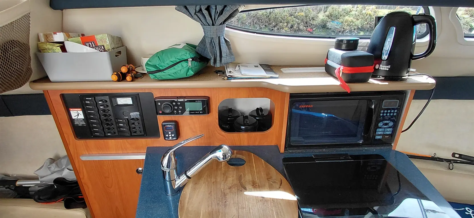 Interior of a boat featuring a kitchen area with a sink, microwave, kettle, storage compartments, and documents on the counter.