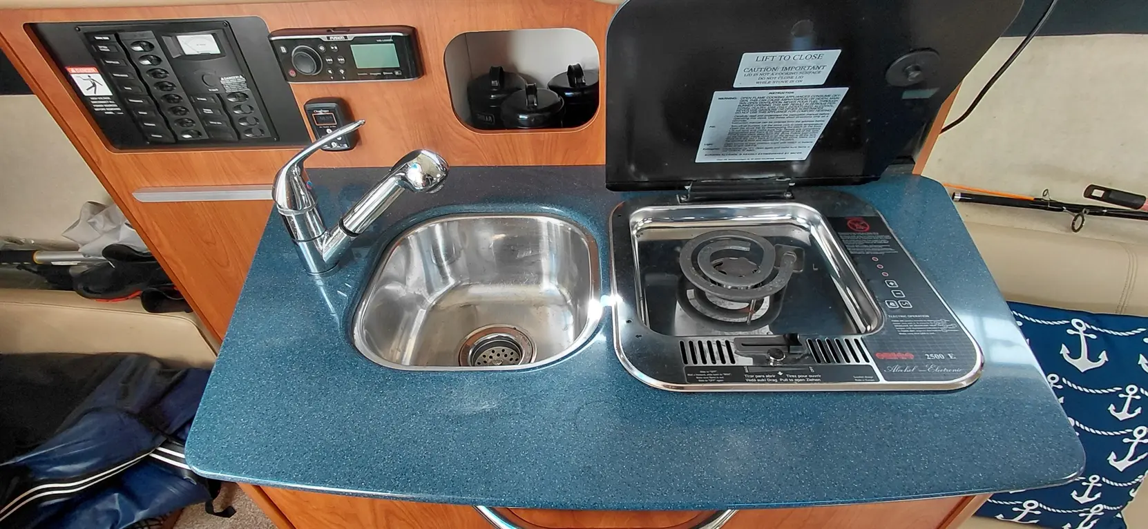Compact kitchen area featuring a stainless steel sink, gas burner, control panel, and storage for kitchen items.