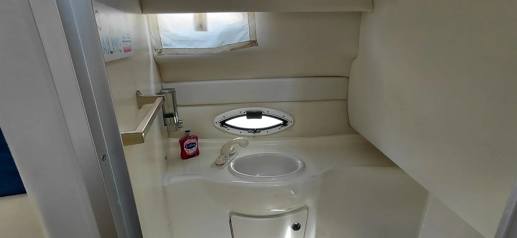 Compact marine bathroom featuring a sink, soap dispenser, porthole, and light-colored walls, ideal for boating adventures.
