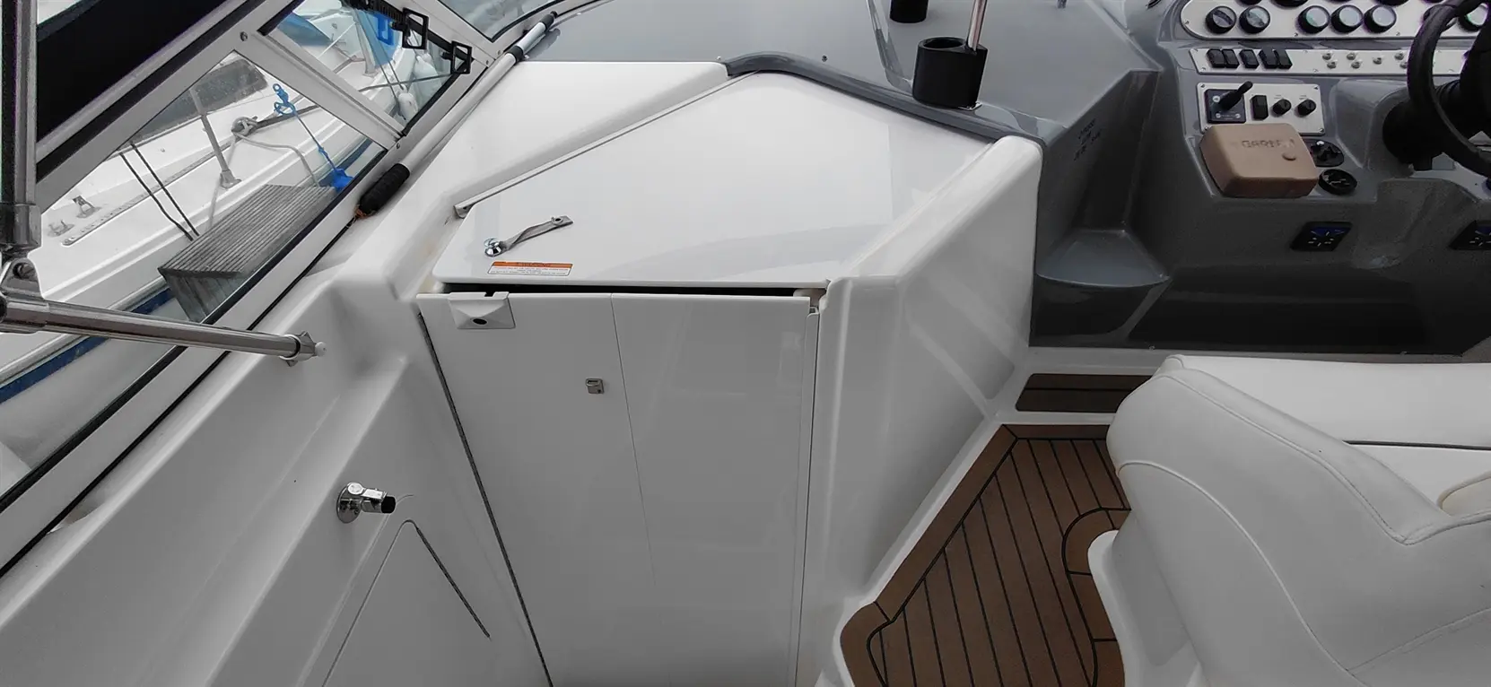 A boat cockpit featuring white cabinetry, a helm with controls, and a padded seat on wooden flooring.