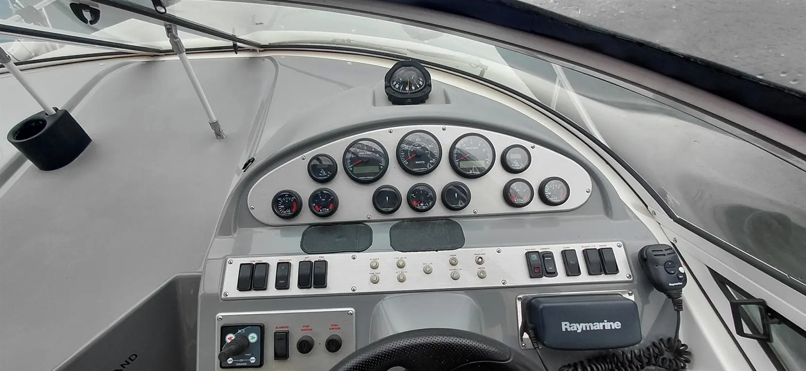Boat dashboard with gauges, controls, and a Raymarine device, showcasing navigation and monitoring equipment.