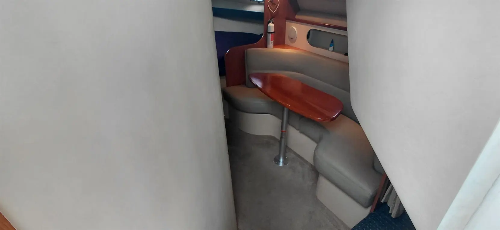 Interior view of a boat's seating area, featuring a wooden table and curved gray benches against a light wall backdrop.