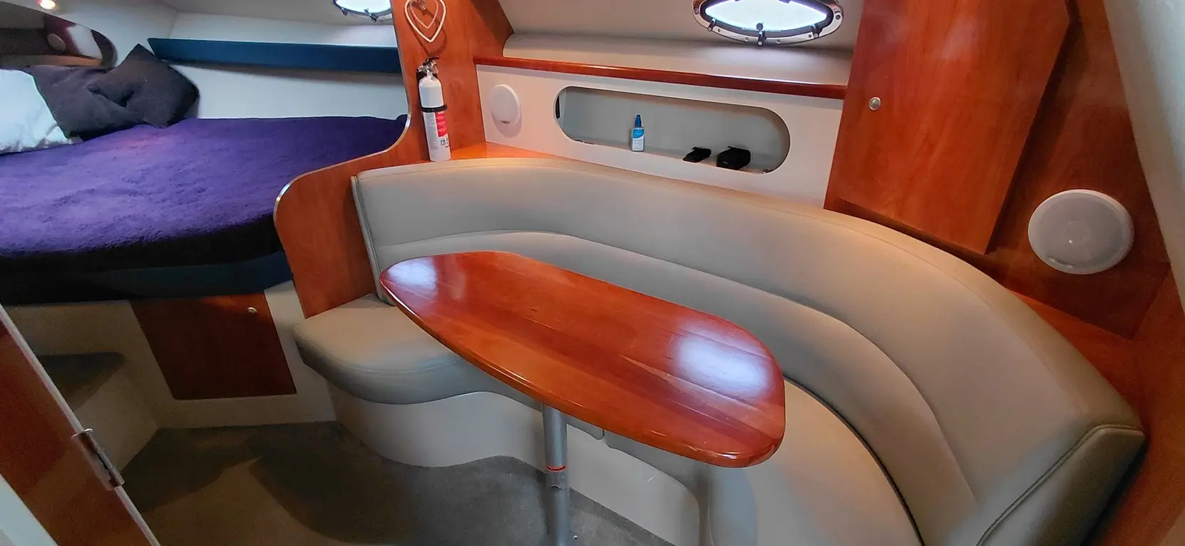 Interior of a boat cabin featuring a cozy seating area, wooden table, and a double bed with purple bedding.