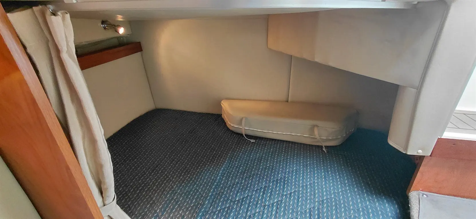 Interior cabin of a boat with blue patterned flooring, a light fixture, and a beige cushion on the floor against the wall.