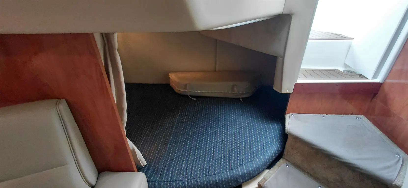 Interior of a boat showing a cozy sleeping nook with blue patterned carpet, wooden walls, and a small mattress.