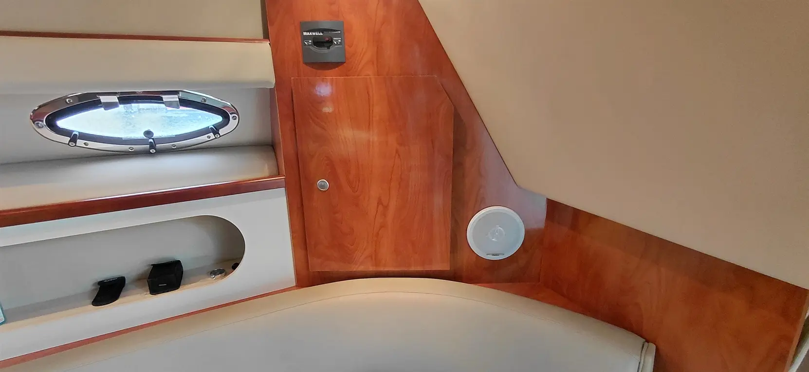 Interior view of a boat featuring a round window, wooden paneling, and a circular speaker near a curved seating area.