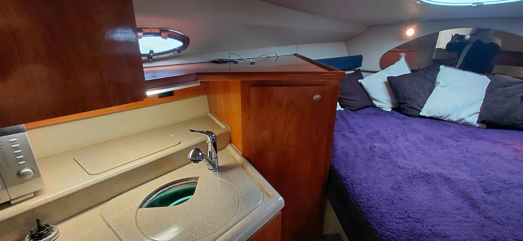 Compact cabin interior featuring a silver faucet, small kitchenette area, purple bedding, and decorative pillows.