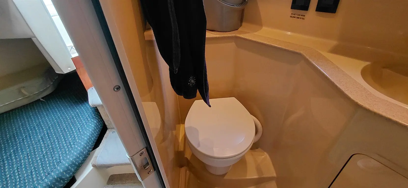 Compact marine bathroom featuring a white toilet, towel hanging, and a glimpse of textured blue fabric flooring.
