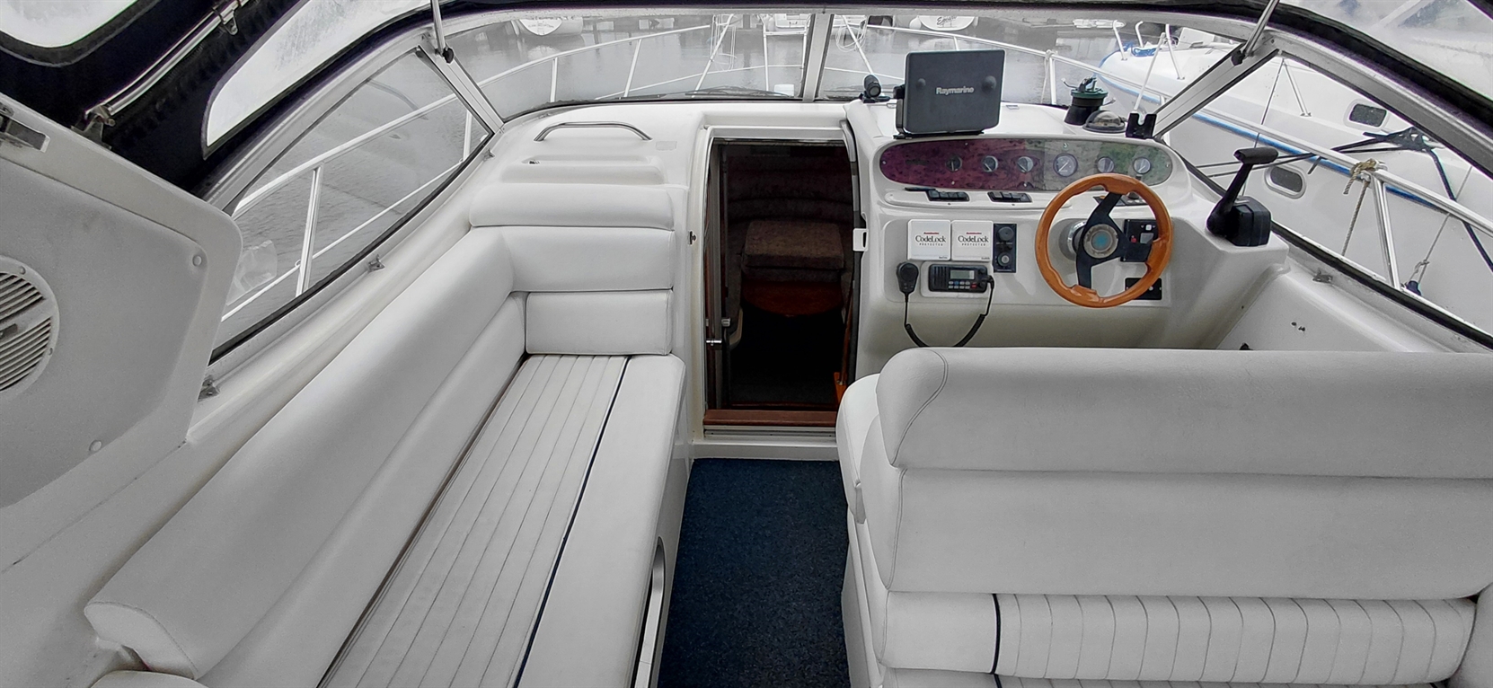 Interior view of a boat cabin showing white leather seating, dashboard controls, and a doorway leading to a cozy space.
