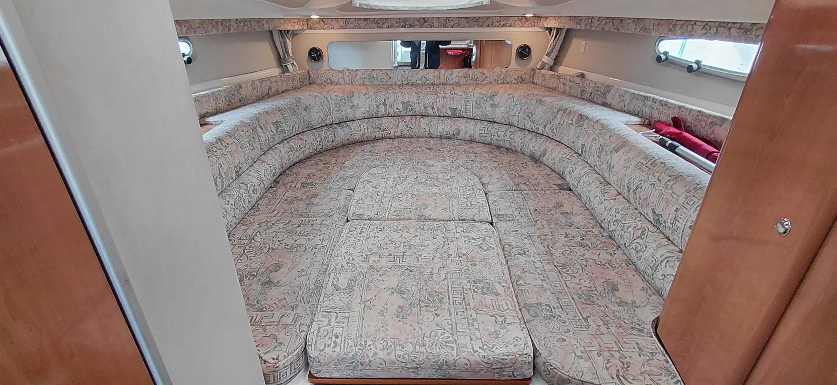 Interior of a boat featuring a spacious circular seating area with patterned upholstery and a wooden door.