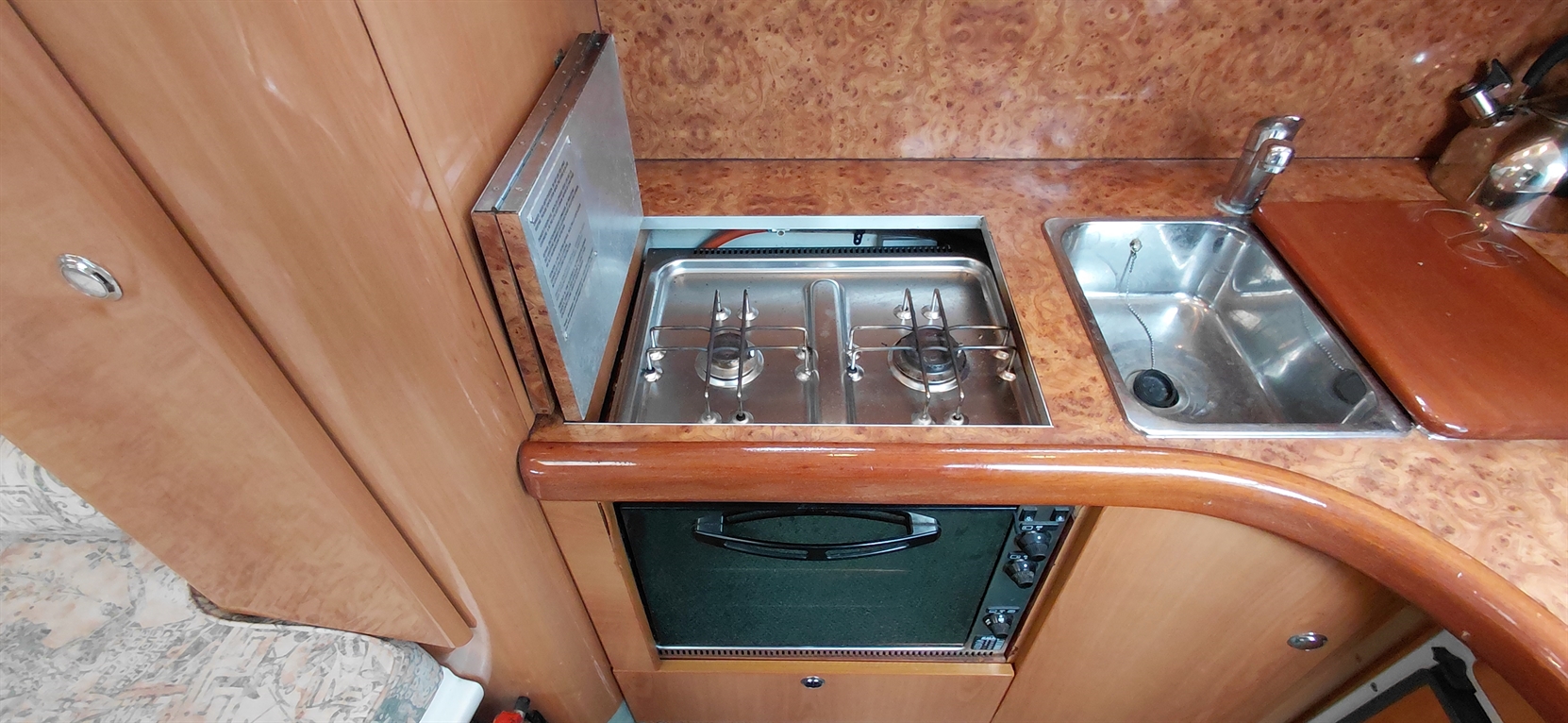 Compact boat kitchen featuring a two-burner stove, stainless steel sink, and an oven beneath a wooden countertop.