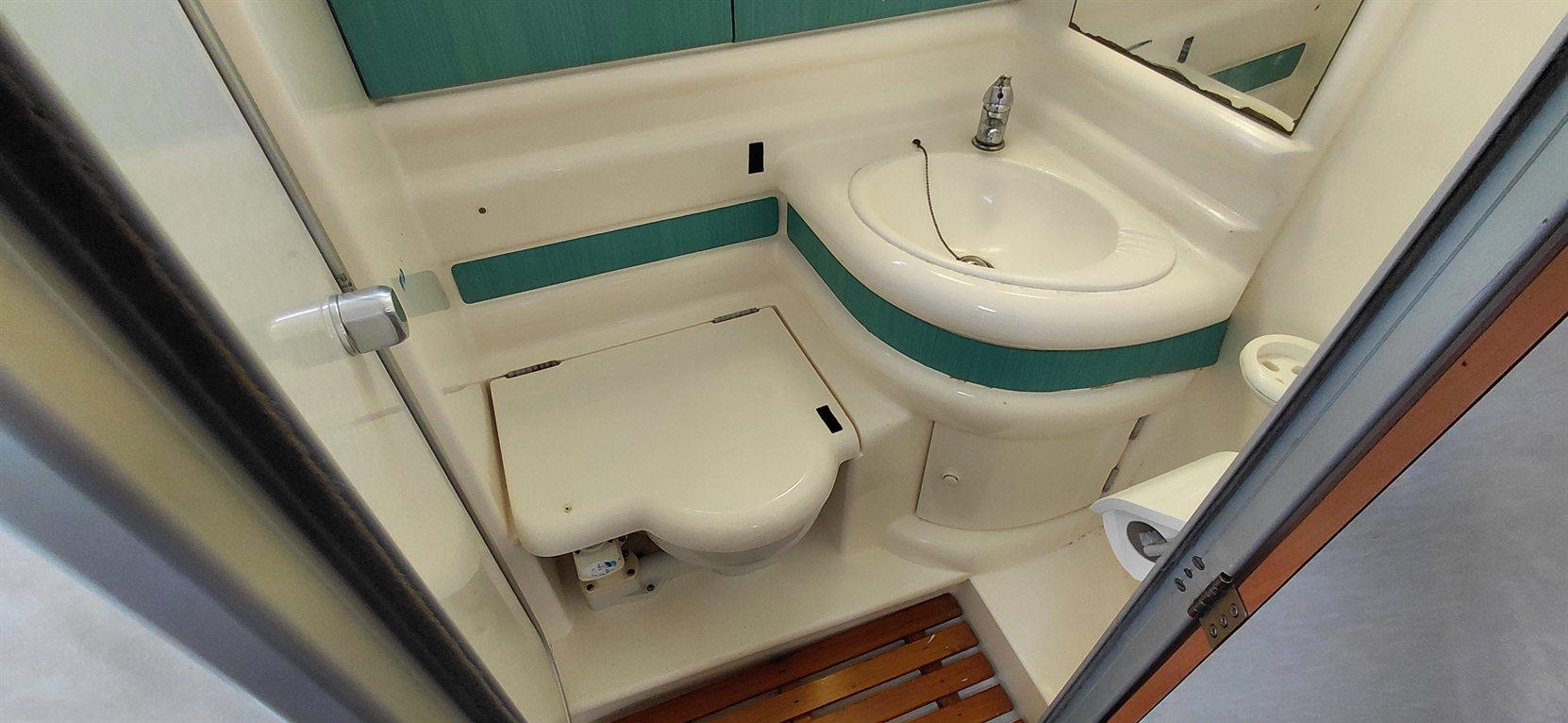 Compact bathroom with a toilet, sink, and green accents, featuring wood flooring and a mirror.
