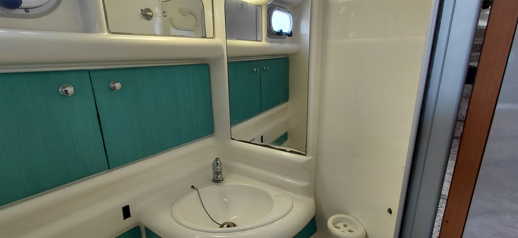 Brightly colored boat bathroom featuring a sink, mirror, and small storage cabinets against a teal wall.