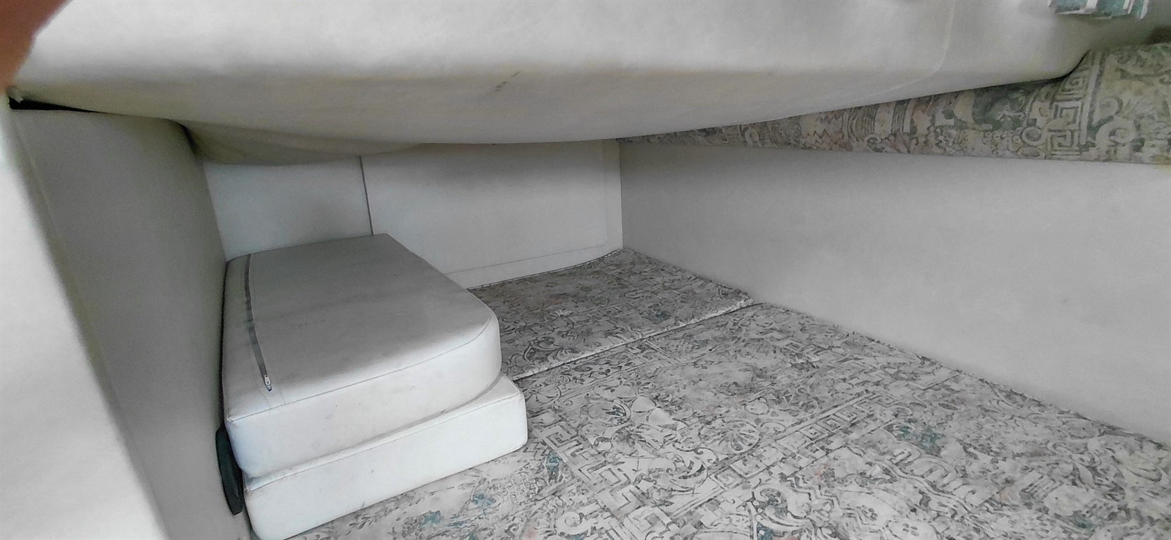 Interior view of a small room or storage space with white cushions and a patterned floor.