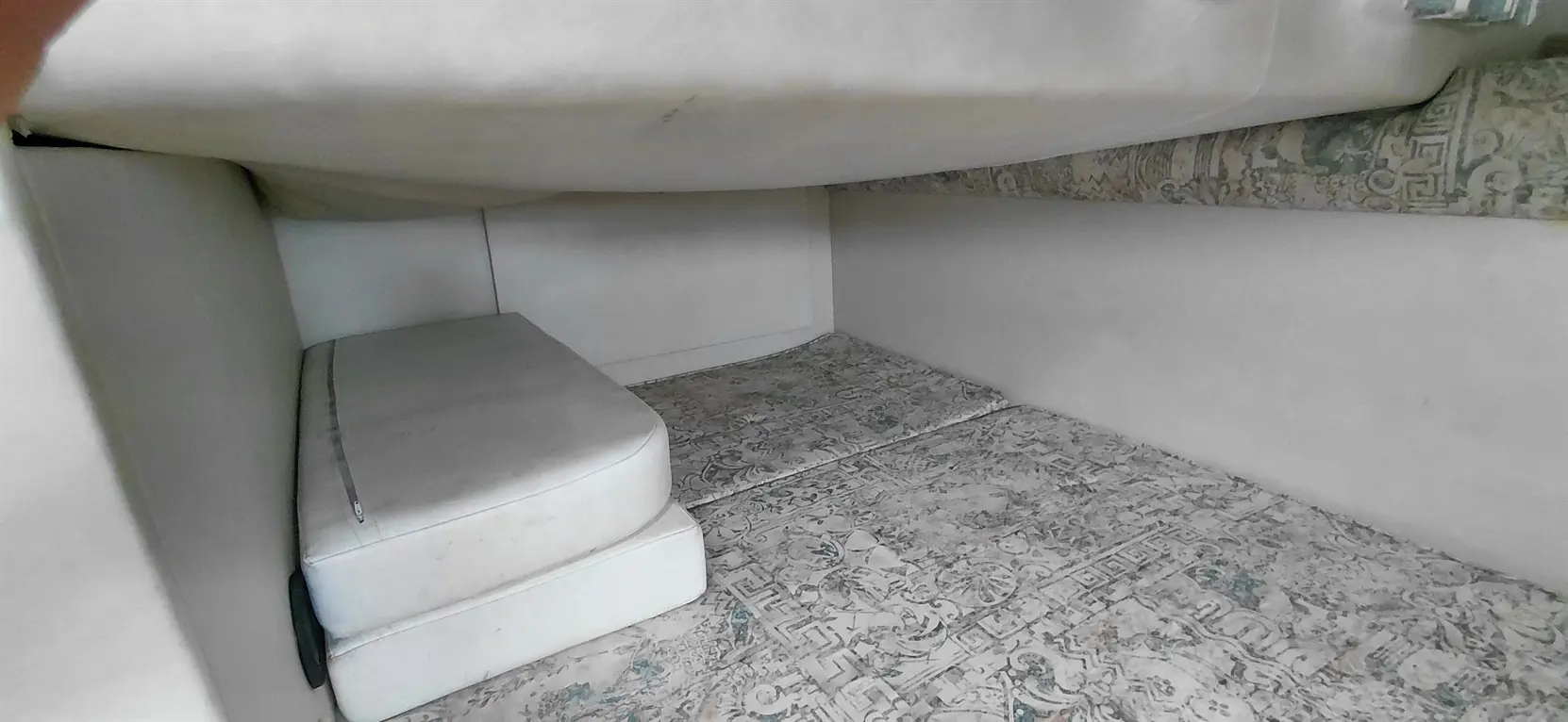 Interior view of a small room or storage space with white cushions and a patterned floor.