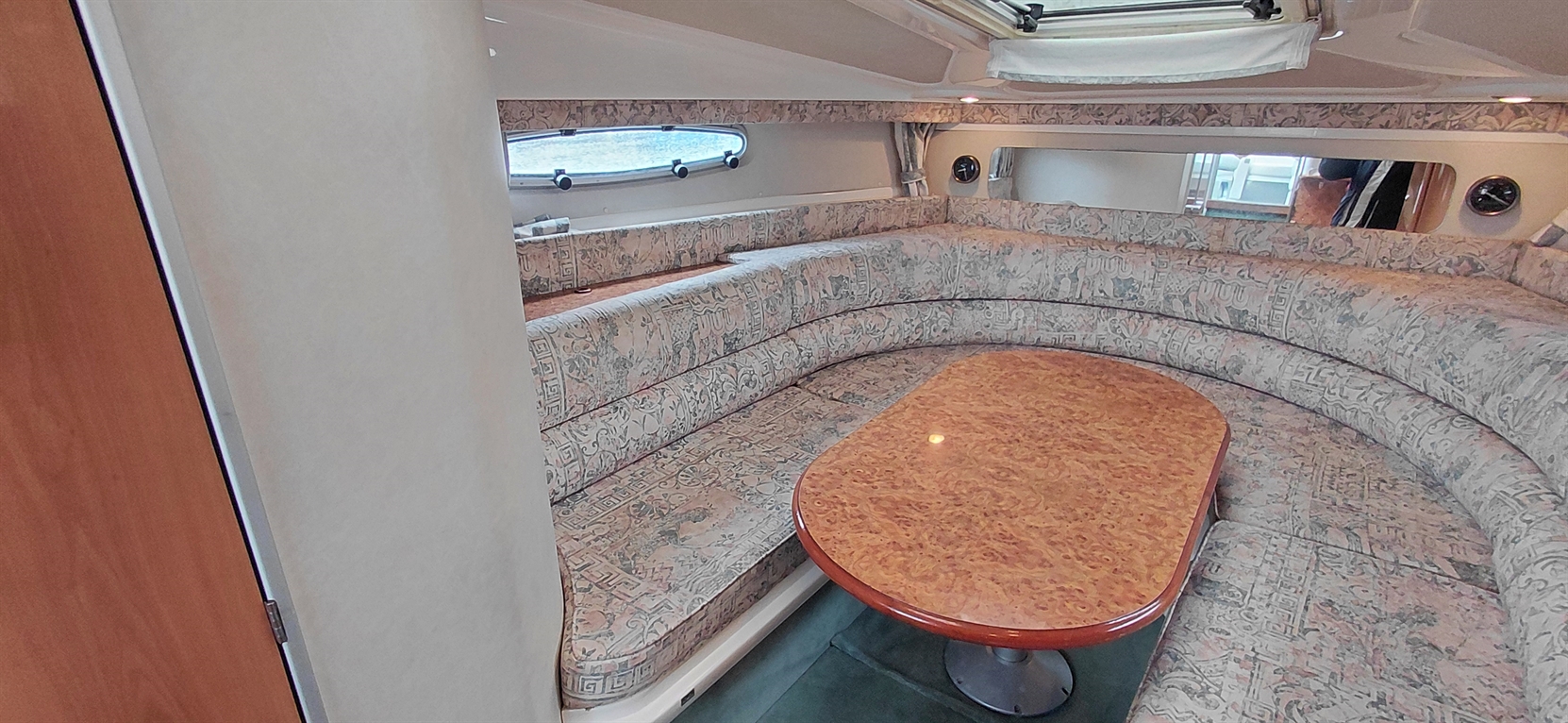 Cozy interior of a boat featuring a circular seating area with patterned upholstery and a wooden table in the center.