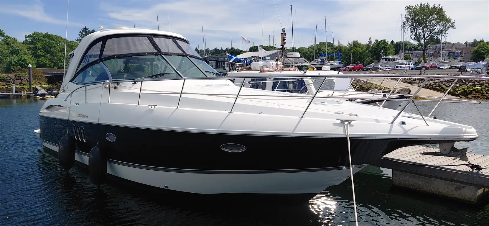 A sleek white and black cabin cruiser yacht docked at a marina, surrounded by other boats and a clear blue sky.