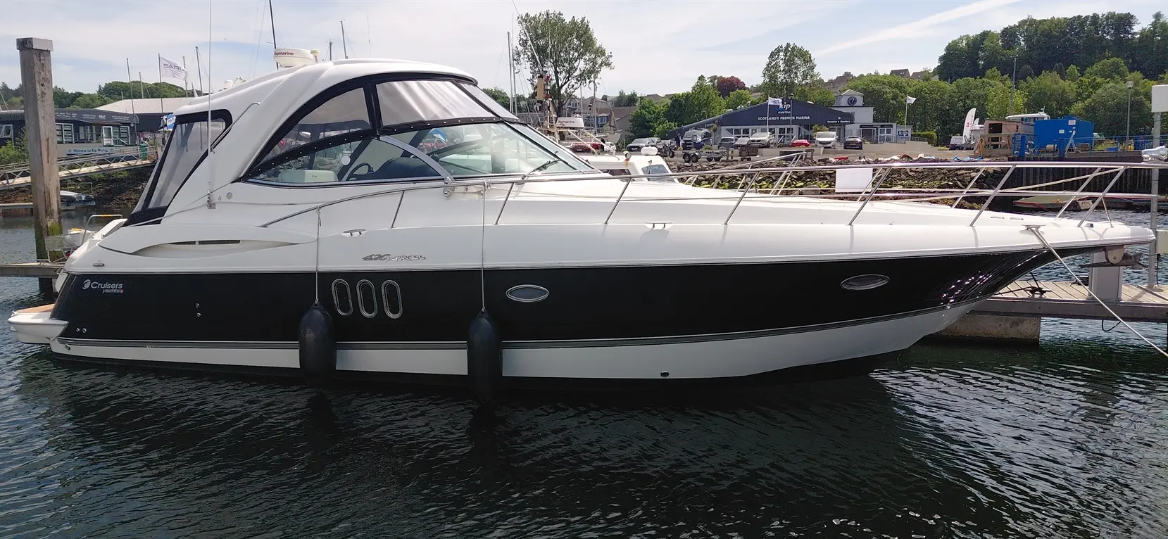A sleek black and white Cruisers yacht docked at a marina, reflecting light on calm waters, surrounded by other boats.