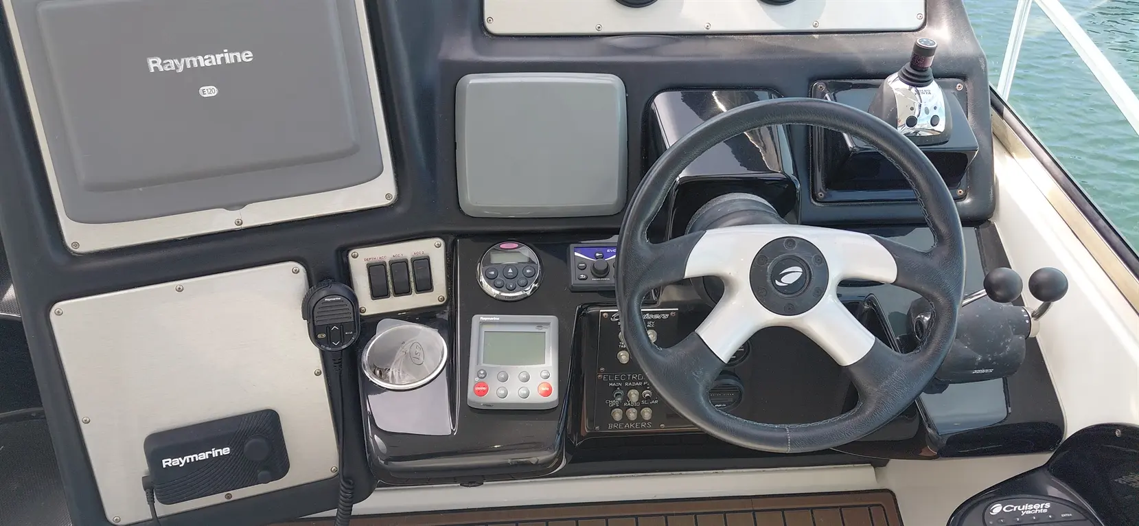 Boat dashboard featuring a Raymarine display, steering wheel, various controls, and navigation devices.