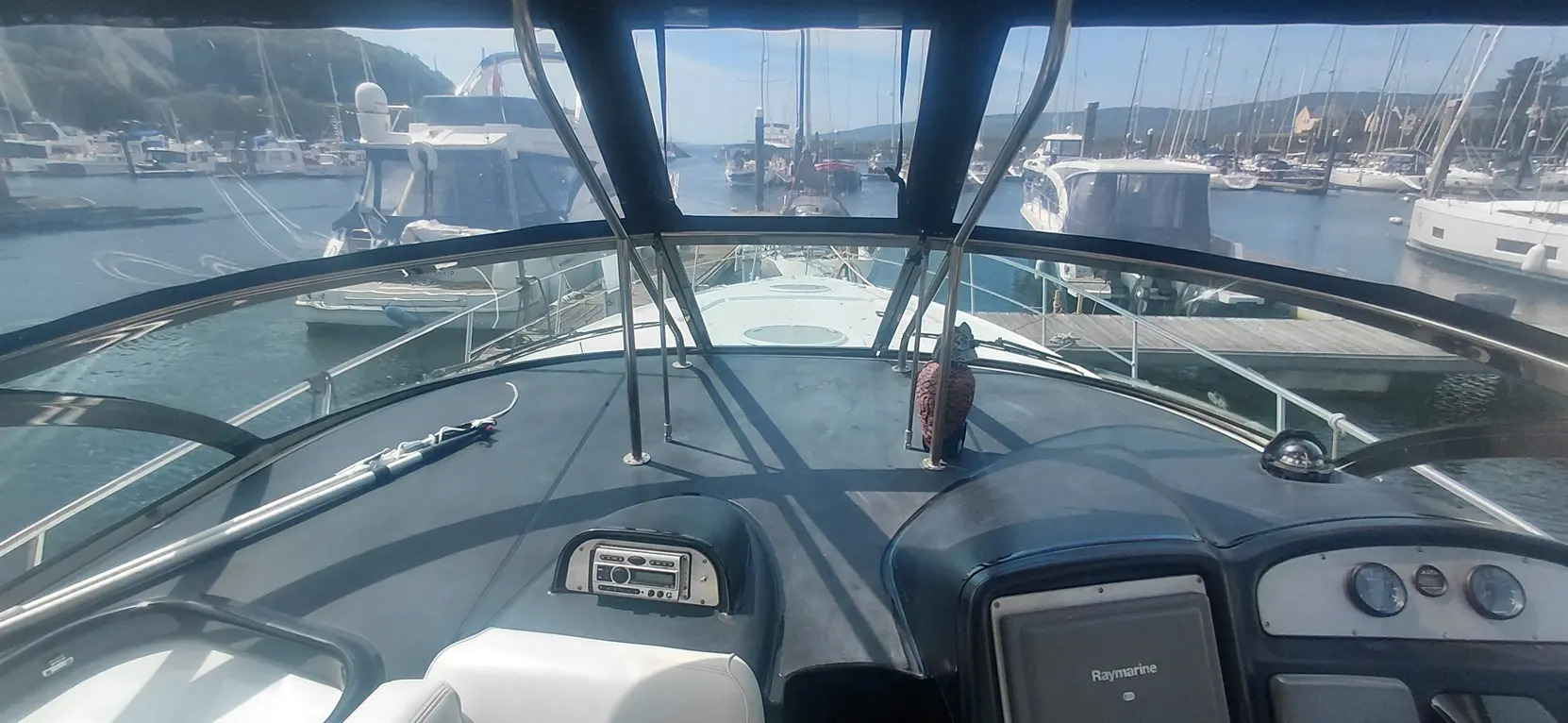 View from the helm of a boat, showcasing the controls and dashboard with a marina filled with moored boats in the background.